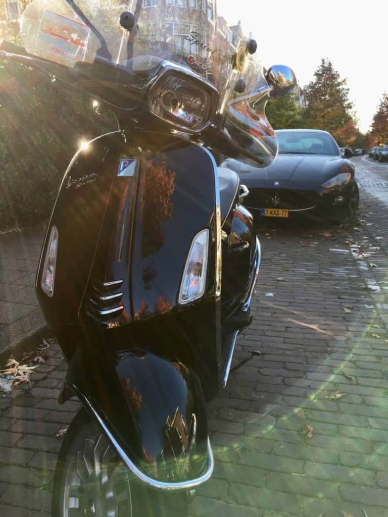 Black Vespa Sprint 50cc in front of a black Maserati