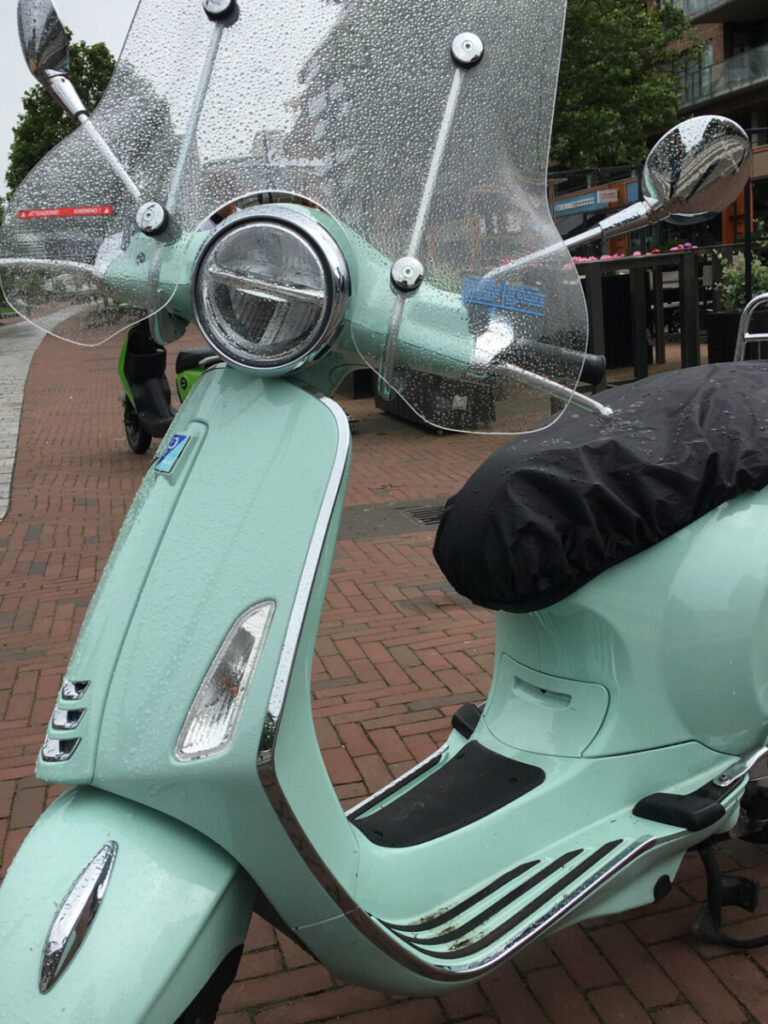 Green Vespa Primavera in the rain with high windshield