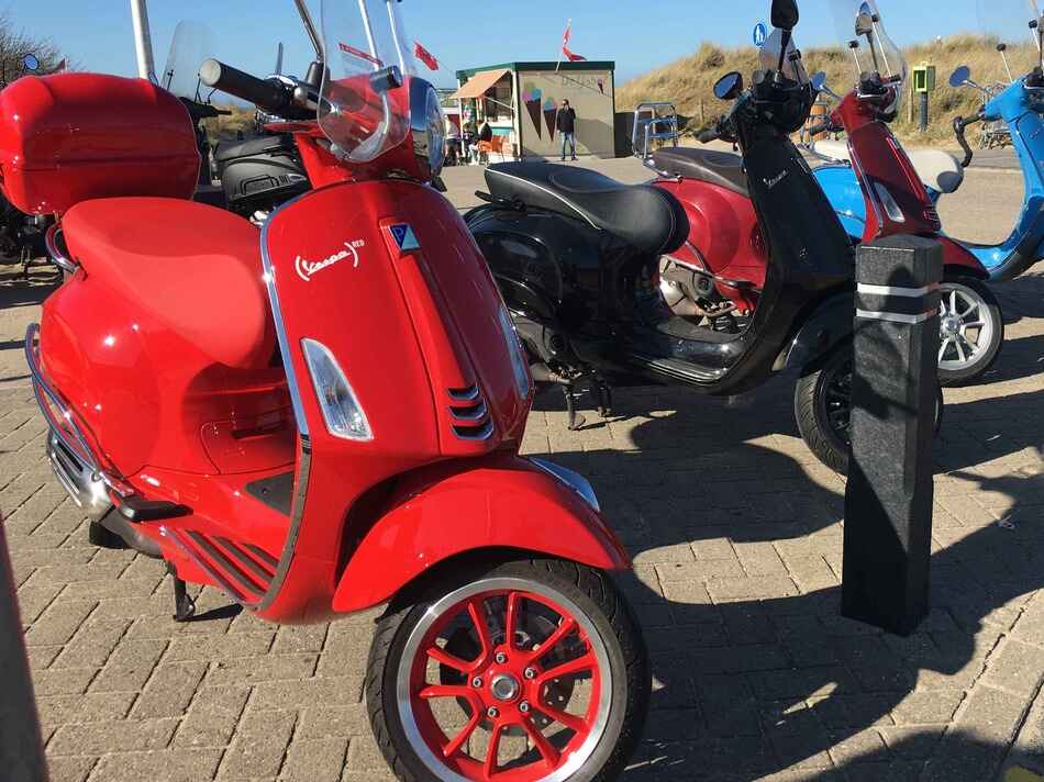 vespa red parked next to three other vespa primavera's